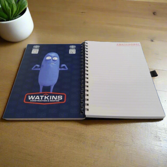 Notebook with blue cover featuring a cartoon character and 'Watkins' branding, open to reveal white pages.